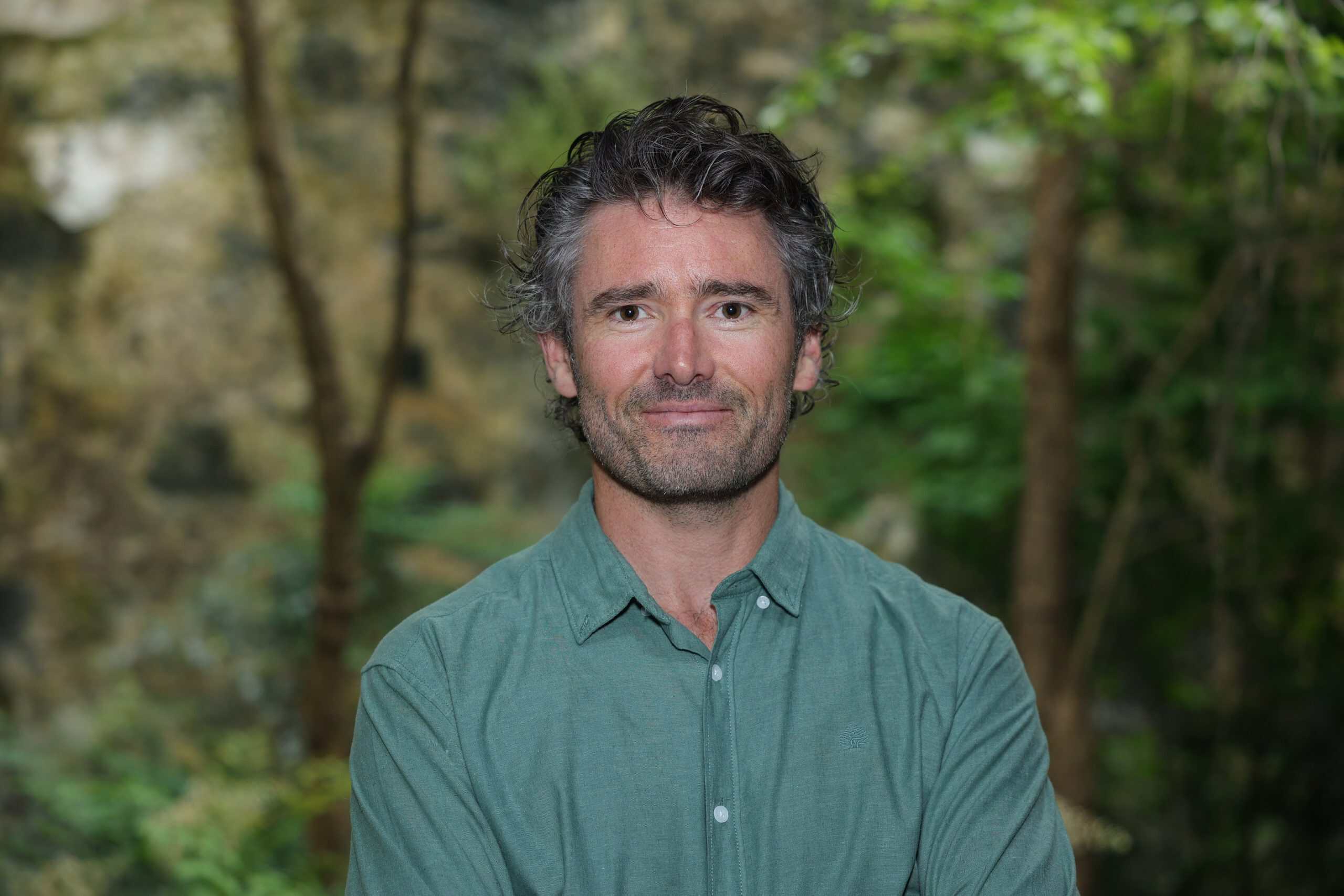 Professional man outdoors with a blurred green forest background, representing creative and outdoor branding services.