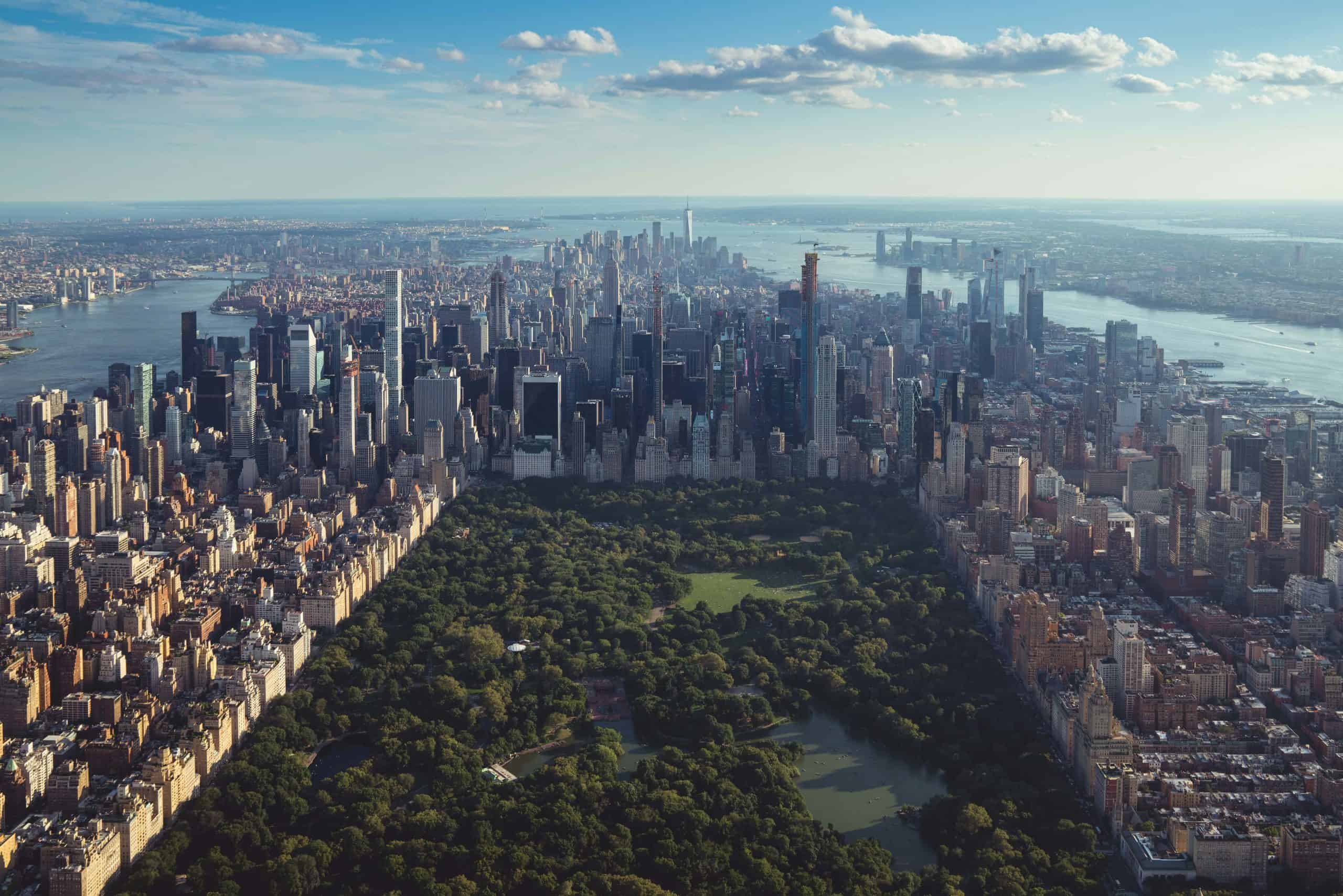 Aerial view of New York City skyline with Central Park in foreground and Manhattan skyscrapers in background, showcasing urban architecture and cityscape.