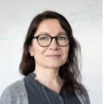 Experienced professional woman with glasses and dark hair in a modern office environment.