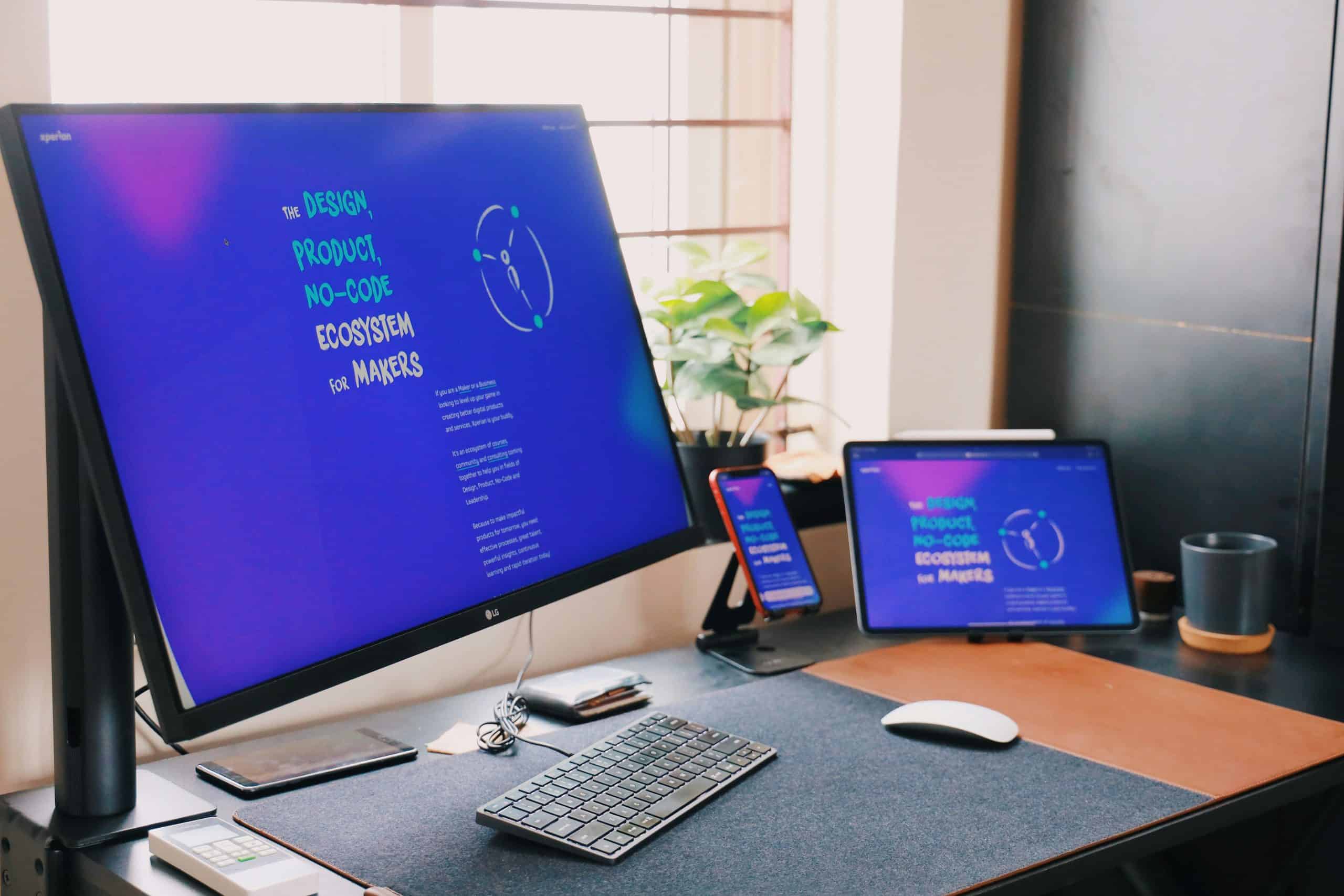 Workspace with large monitor, tablet, smartphone, and keyboard for digital design.